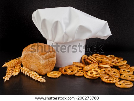 Wheat Bread, Pretzels and  Chef Hat on black table background
