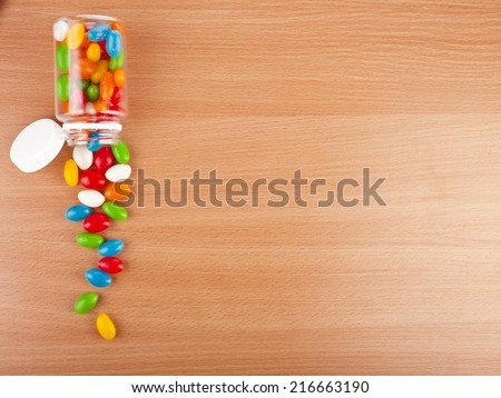 Colored Pills spilled from a bottle  on surface wooden table. top view