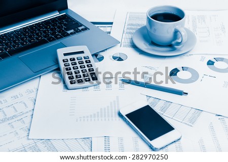 Close of business workplace with financial reports and office stuff.  Blue toned