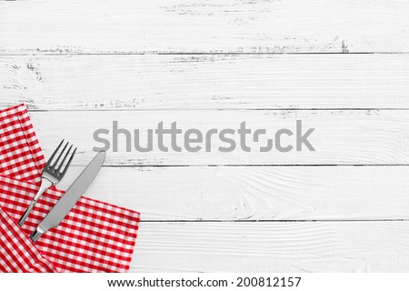 knife and fork with red checked tablecloth and copyspace on white old vintage wooden table