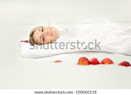 Young blond woman is lying in the snow. Some apples are near her.
