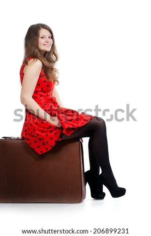 A beautiful woman is sitting on a luggage. Isolated on a white background