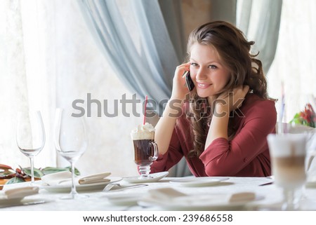 A smiling woman in restaurant is talking to mobile phone