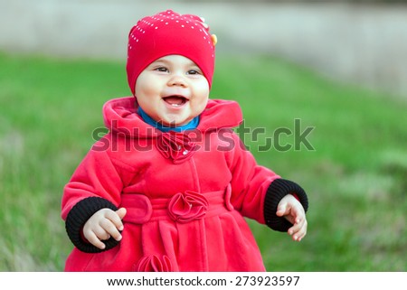 Little smiling girl in red coat is posing on the lawn