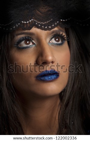 Beautiful woman with brown eyes, blue makeup and lips, and head covered in black lace staring upwards