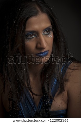 Beautiful woman with blue makeup, blue dress and gems on her face glancing sideways