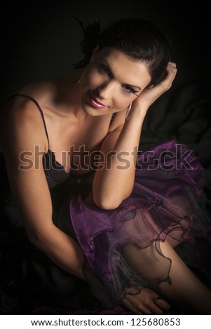 Beautiful dark haired woman with purple dress and makeup sitting with head in hand