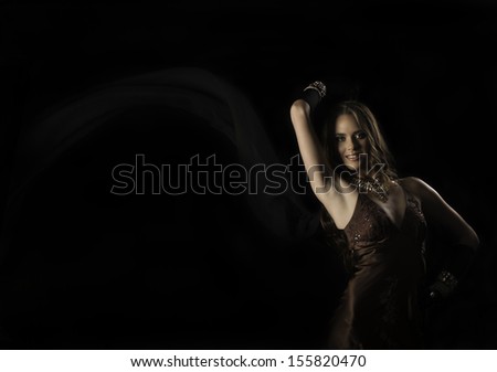Beautiful brunette woman in vintage evening dress and long gloves, holding up a chiffon scarf blowing in the breeze against a black background