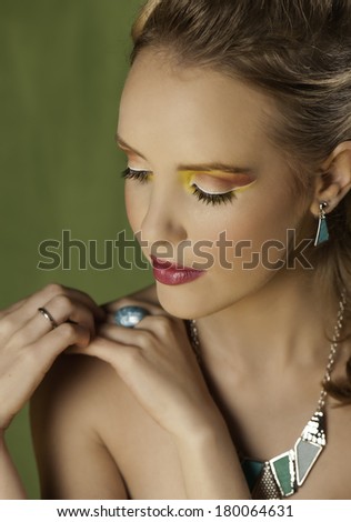 Portrait of sensual blonde woman wearing graphic and colorful makeup with turquoise and silver jewelry, looking down and seeming lost in thought