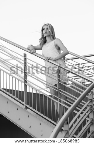 Monochrome portrait of a beautiful blonde urban woman leaning against the rail of a staircase in an urban setting while gazing far away