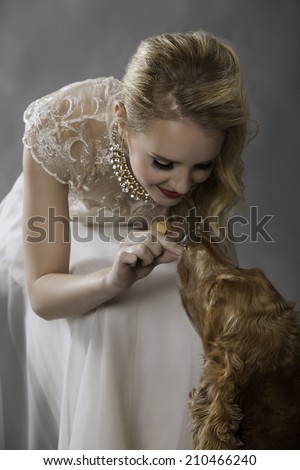 Portrait of lovely blonde woman in vintage dress feeding her cute golden Spaniel dog a treat while smiling affectionately at her pet