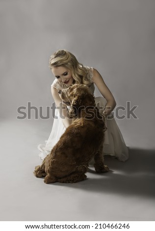 Glamorous blonde woman in vintage dress playing affectionately with her adorable dog