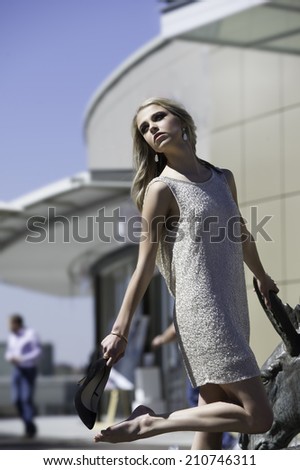 Portrait of gorgeous young woman wearing sparkling cocktail dress standing in an urban setting while putting on her black pump shoes