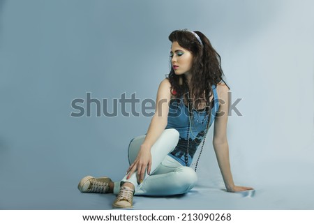 Attractive brunette woman with turquoise eighties outfit, eighties colorful makeup and jewelry, wearing funky gold sneakers