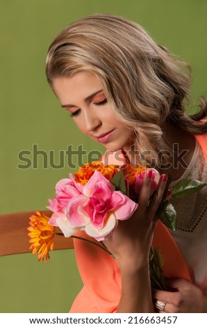 Portrait of gorgeous blonde girl wearing her long hair in side swept curls looking down to the bouquet of spring flowers in her hand