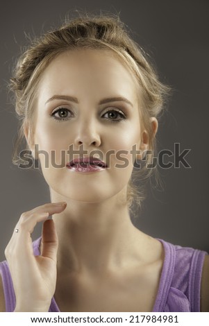 Portrait of lovely blonde woman with natural makeup and plum lips holding her hand to her face