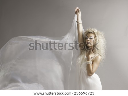 Blonde fairy woman in white standing with white material blowing in the breeze