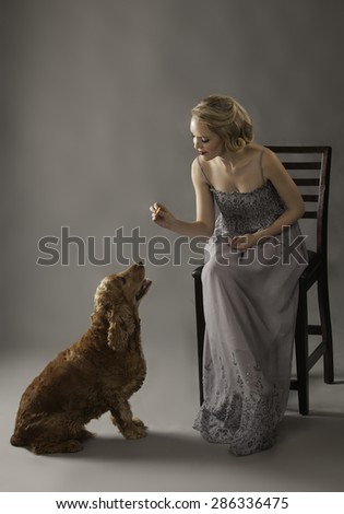 Lovely seated woman holding out a treat to a cute dog at her feet