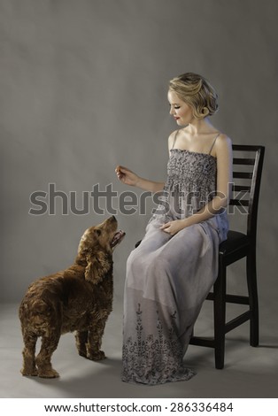 Pretty blonde woman holding out a treat for the cute dog at her feet