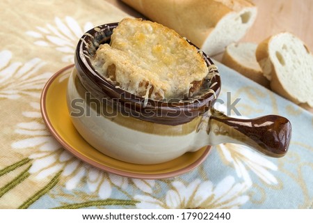 Traditional crock full of French onion soup topped with melted gruyere and served with French bread