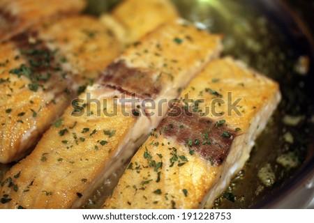 Salmon, dipped in pan searing flour, is pan seared in olive oil with parsley flakes.