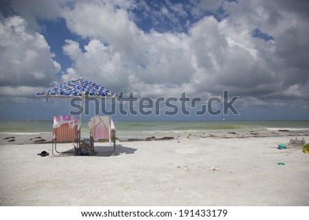 A view from the beach into the Gulf of Mexico from Honeymoon Island State Park in Dunedin, Florida. Two beach chairs are set up with an umbrella in between.