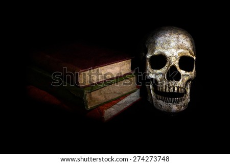 A vintage skull sits beside a stack of old novels; image created with a light painting technique