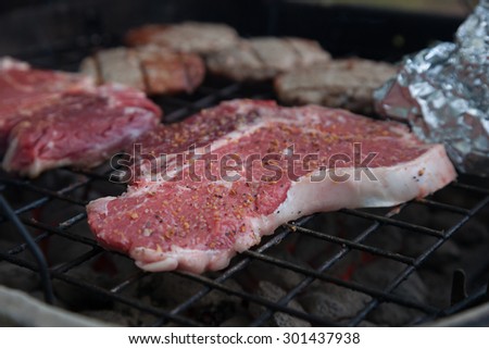 T-bone steaks sit smoking with other food on a charcoal grill