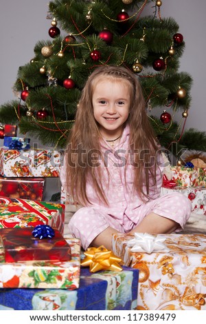 Girl in pajamas sitting under the Christmas tree with gift in hand