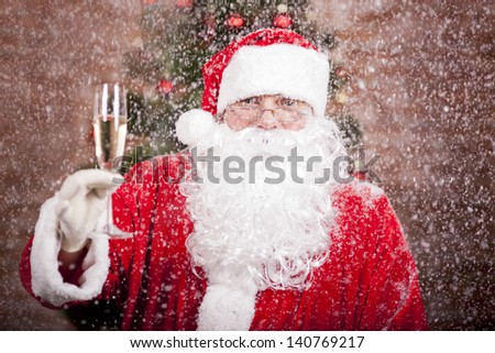 Santa Claus with a glass of sparkling wine champagne under snowfall near a Christmas tree