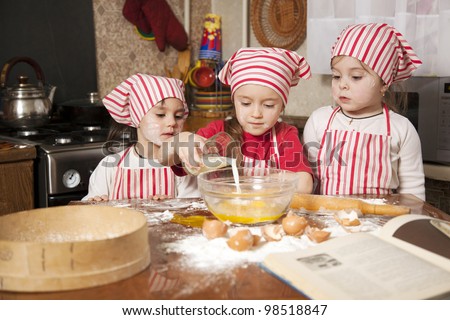 Three little chefs enjoying in the kitchen making big mess. Little girls making bread in the kitchen