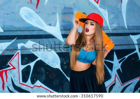 Beautiful girl with skateboard posing against graffiti wall. Attractive caucasian skater woman