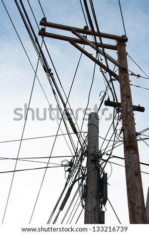 Electrical, telephone and cable lines are tangled on two adjacent utility poles.