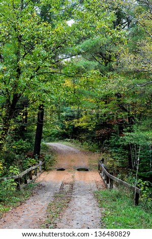 This winding New England road crosses a small stream via a bridge.  It is early fall, with the foliage just beginning to turn, and a light rain has left puddles in the road.