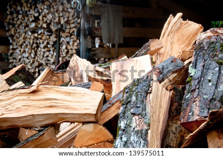 A pile of cord wood is ready to be stacked in the woodshed. In the background is already stacked wood.