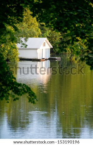 A country boat house glows in the sun on a still evening.