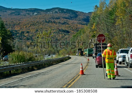 Bolton, VT, USA - October 9, 2013: A traffic control  worker stops traffic on Vermont  State Highway 2 during a paving project on a clear autumn day while cars stream by on the adjacent Interstate 89.