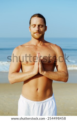 Athletic Man with No Shirt doing Yoga at the Beach showing Namaste welcome gesture with closed eyes
