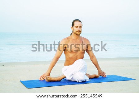 Long Hair Athletic Man with No Shirt doing Yoga on Blue Mat at the Beach\
Cow Face Pose - Gomukhasana