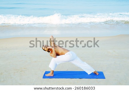 Long hair athletic man with no shirt doing yoga on blue mat at the beach