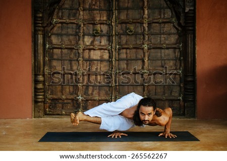 Indian ethnicity young man wit a strong body showing difficult yoga pose (Eight Angle Pose - Astavakrasana) in front of old oriental style door.