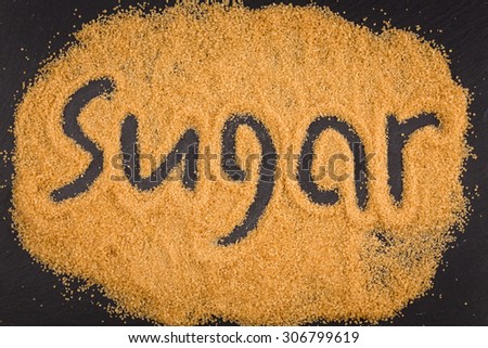 word sugar written in brown granulated sugar on dark stone background