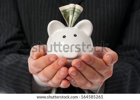 Man holding white piggy bank with dollar inside over black suit background.