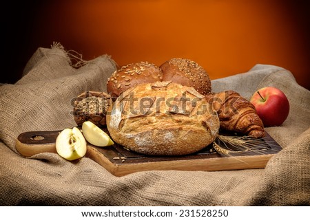Assortment of baked bread with wheat and apples arranged on coarse textured woven fabric