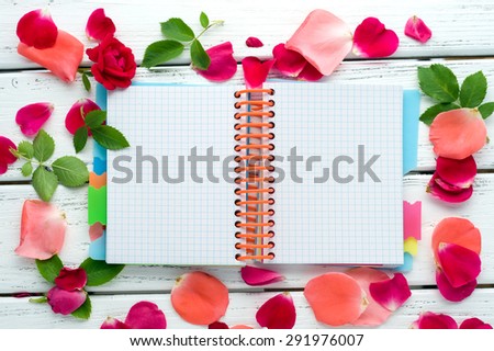 Blank notepad with rose petals over white wooden table. Top view with copy space.