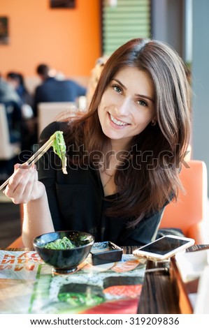 Young smiling woman eating japanese seaweed salad (Chuka) in a sushi restaurant.