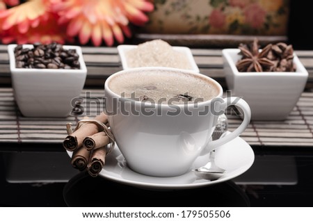 Cup of coffee, spices and coffee beans on black glass surface