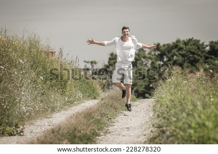 Happy young man with open arms and jumping  in a field  under  the summer  sun
