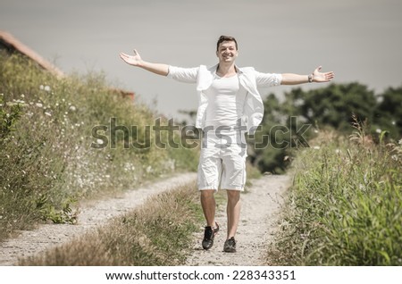 Happy young man with open arms and jumping  in a field  under  the summer  sun