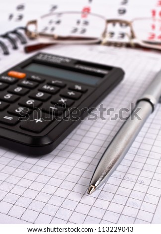 Metallic pen, black calculator, glasses, notebook and calendar